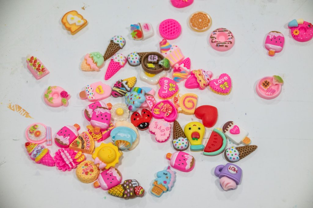 A collection of colorful, small erasers shaped like various desserts and sweets, including ice cream cones, donuts, and cakes, scattered on a white surface.