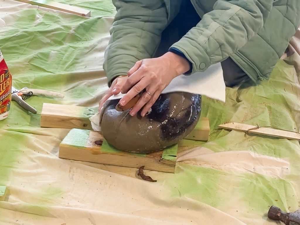 Person cleaning a stone with a cloth on a wooden stand, surrounded by a tarp. A bottle of cleaner is nearby.